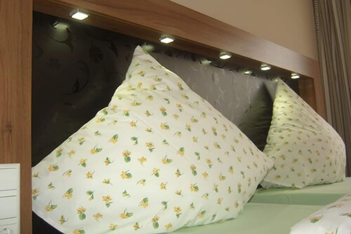 A bedroom with a wooden headboard, two pillows with a floral pattern, and a green bedspread.