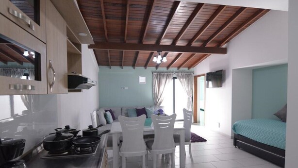 Cocina compacta con armarios blancos, comedor con mesa y sillas, y cama con colcha verde.