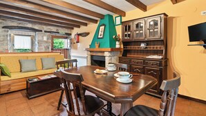 Un coin repas chaleureux avec une table en bois dressée pour deux personnes, une cheminée en pierre et un mur d’accent de couleur verte.