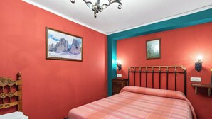 Une chambre à coucher comprenant un lit, une chaise en bois, une table de chevet et une lampe fixée au mur.