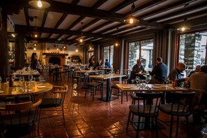 A restaurant with multiple tables and chairs, a brick fireplace, and large windows. - Hotel Mir (Saint-Lary-Soulan)