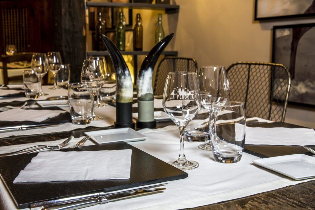 Una mesa de restaurante dispuesta con copas de vino, cubiertos y una carta.