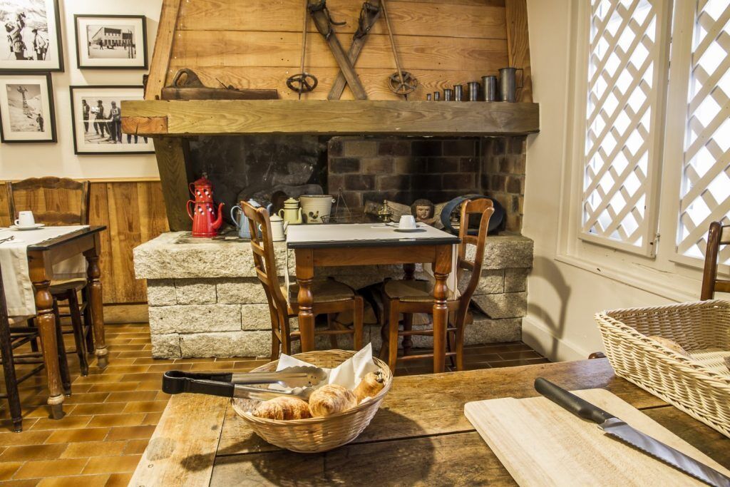 A rustic dining area with a stone fireplace, wooden furniture, and a basket of bread on a table.