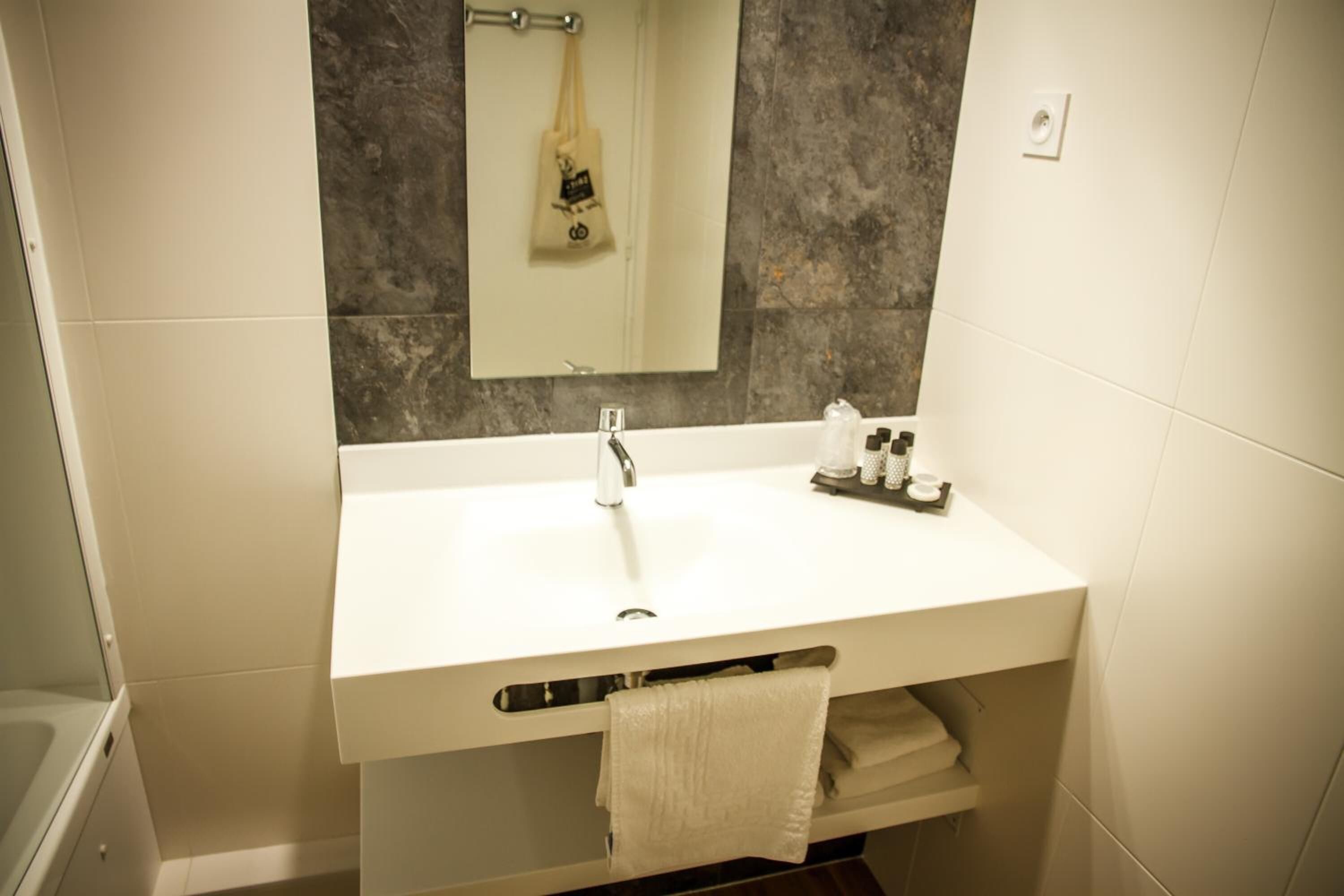 Un baño moderno con un lavamanos blanco, espejo y toallero.