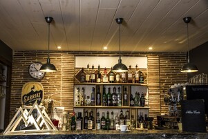 A bar area with wooden shelves stocked with liquor bottles, a clock, and pendant lighting.