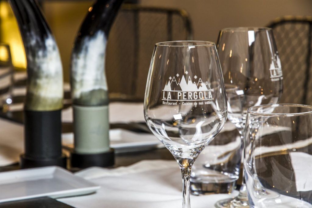 Een gedekte tafel met een wijnglas met de tekst 'LA PERGOLA' en een fles wijn.