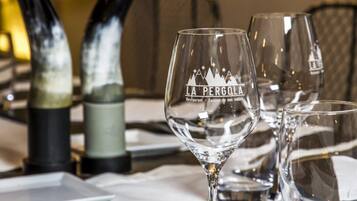 Een gedekte tafel met een wijnglas met de tekst 'LA PERGOLA' en een fles wijn.