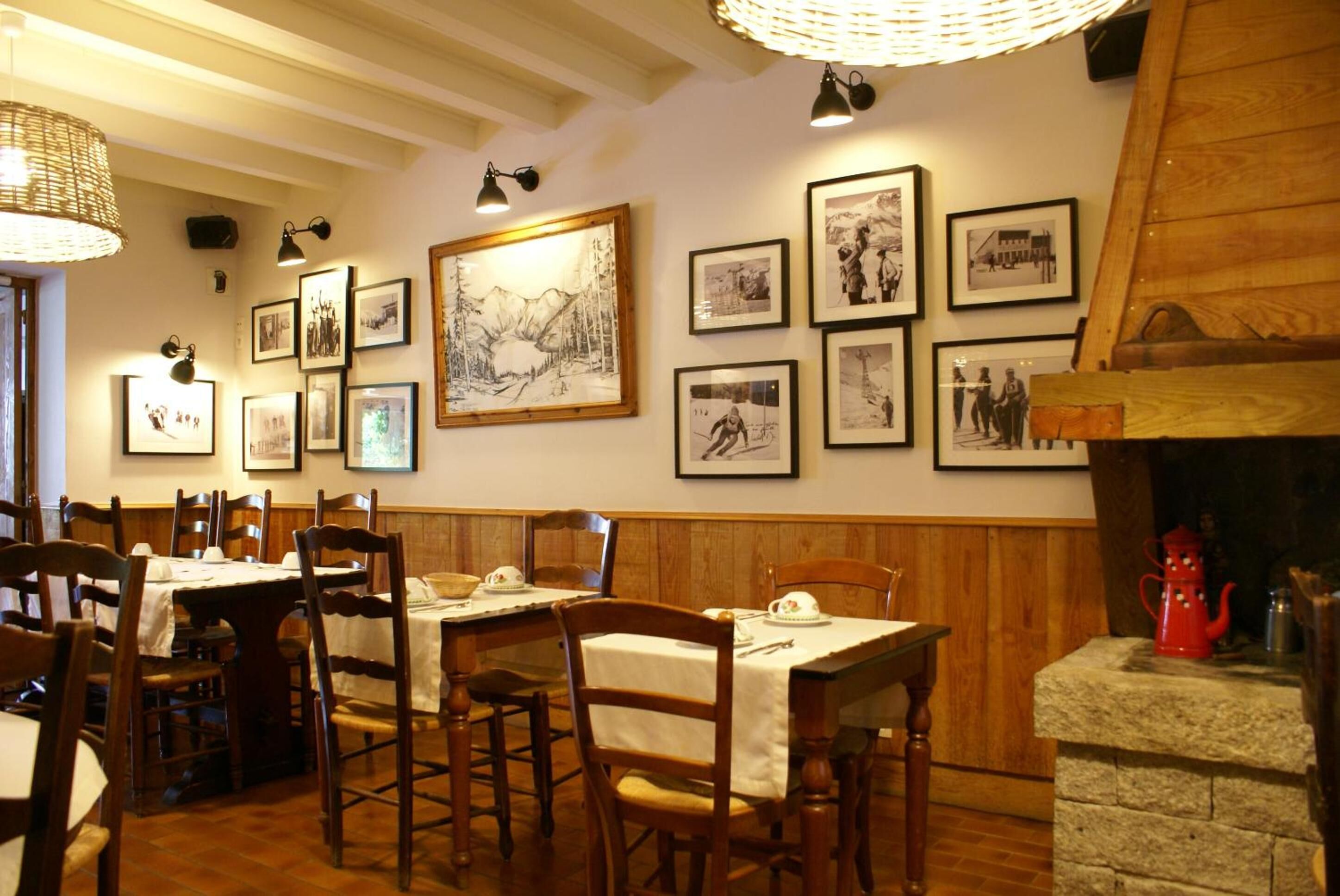 Un espace repas avec des tables et des chaises en bois, des tableaux encadrés au mur et une cheminée en pierre.