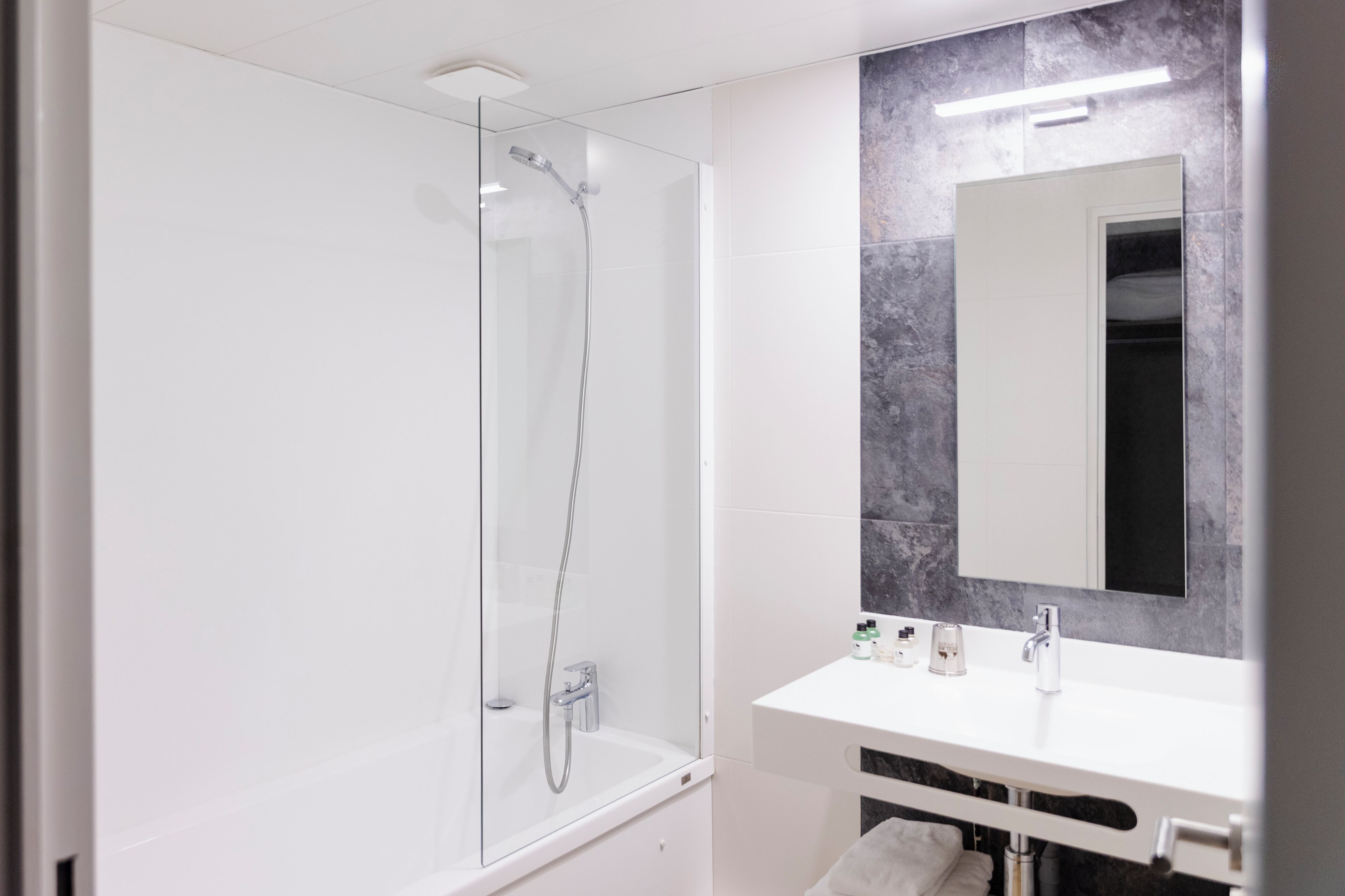 Un baño moderno con ducha envuelta en vidrio, un lavabo blanco y un espejo grande.