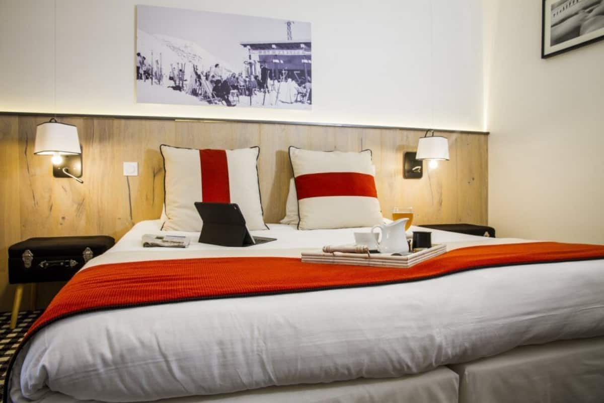 Ein Hotelzimmer mit einem großen Bett, zwei Nachttischlampen, einem gerahmten Bild an der Wand und einer rot-weiß gestreiften Tagesdecke.
