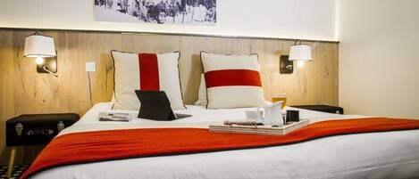 A hotel room with a large bed, two bedside lamps, a framed picture on the wall, and a red and white striped throw blanket.