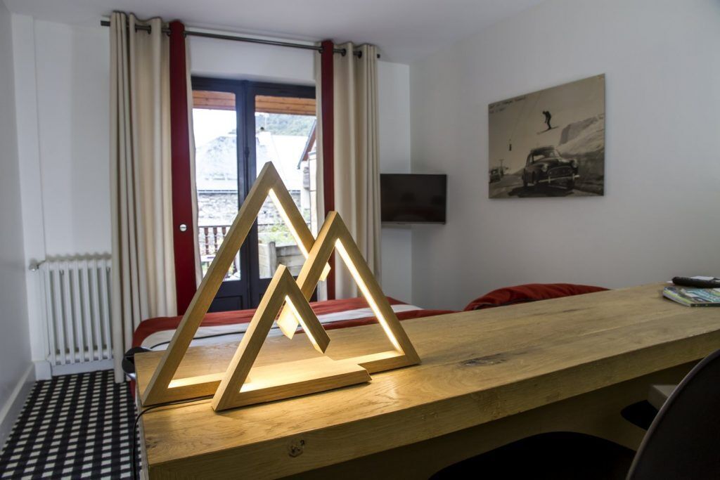 A room with a wooden desk, a television mounted on the wall, and a window with curtains.