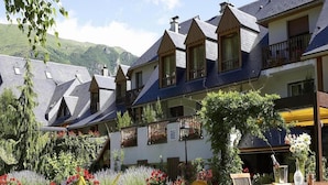 Un pati d'hotel amb mobiliari exterior, jardí i un paisatge de muntanyes al fons.