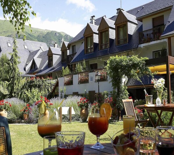 A hotel courtyard with outdoor seating, a garden, and a mountain backdrop. - Hotel Mir (Saint-Lary-Soulan)