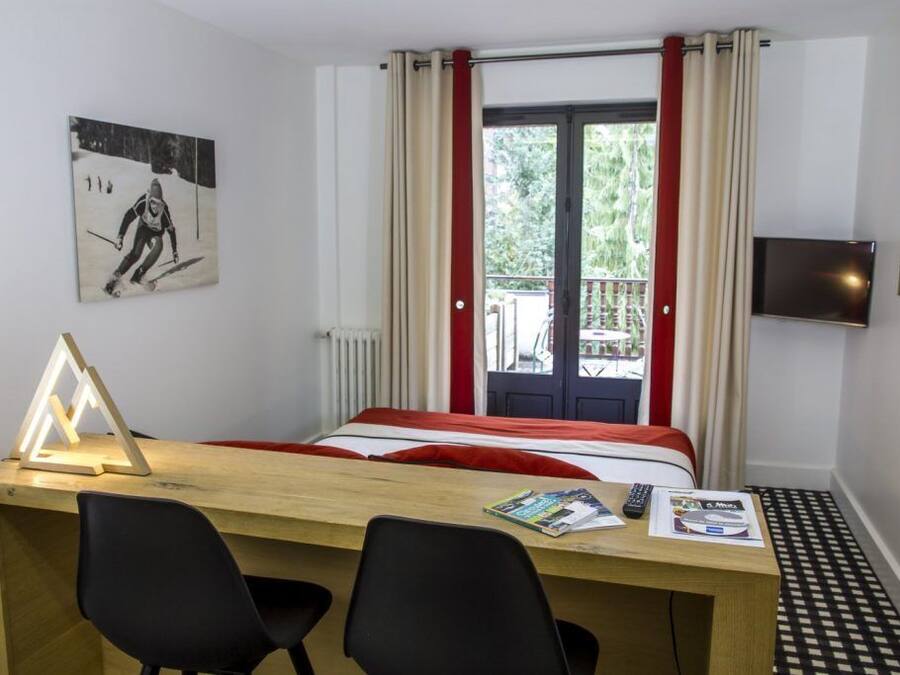 A hotel room with a bed, a desk with two chairs, a TV, and a window with curtains.