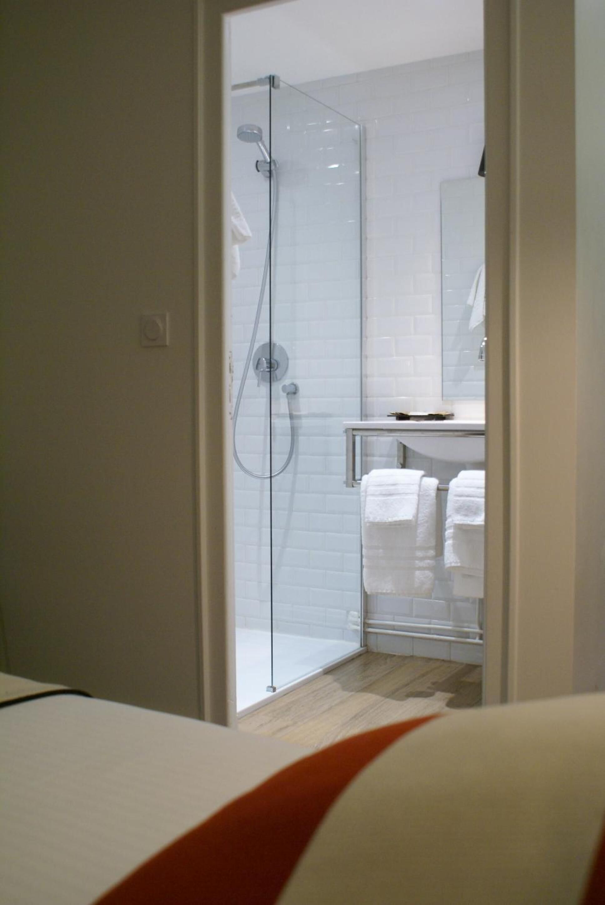 A modern bathroom with a glass-enclosed shower, a white tiled wall, and a visible sink area with towels.