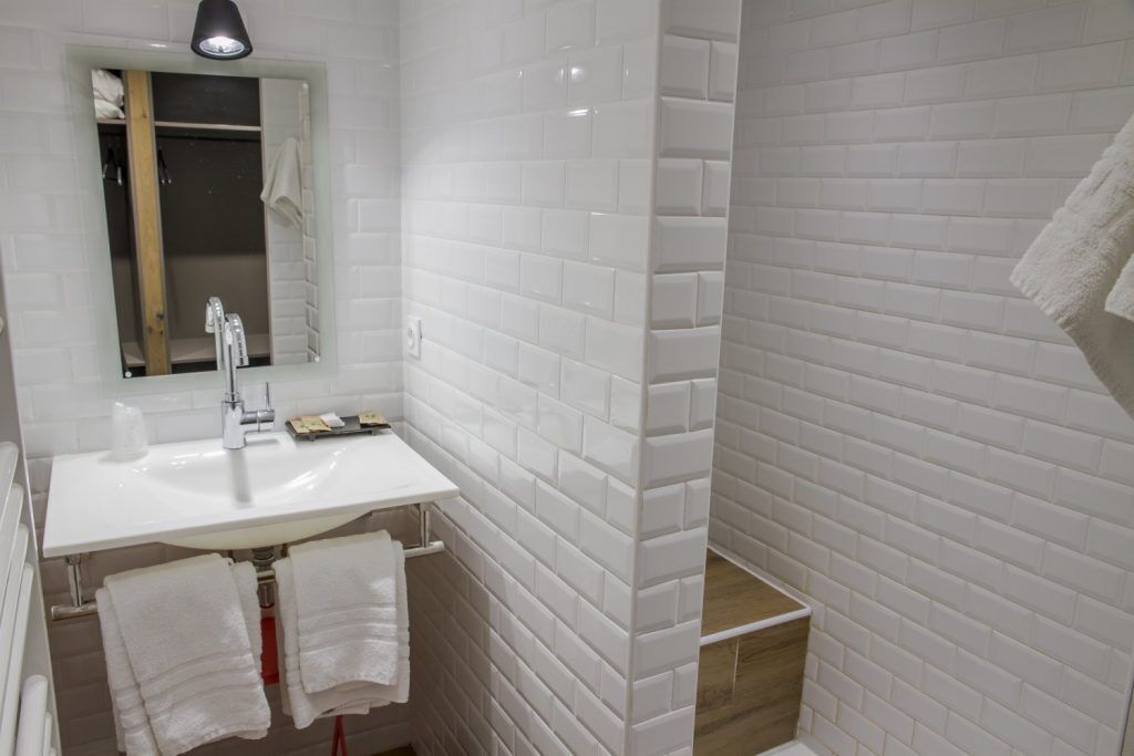 Un bany amb parets revestides de rajoles blanques, un lavabo blanc i dues tovalloles penjades a un suport.
