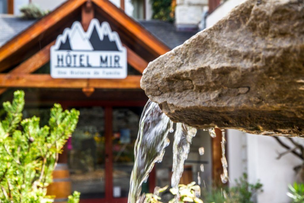 A stone fountain with water flowing from it, in front of a building with a sign that reads "HOTEL MIR."