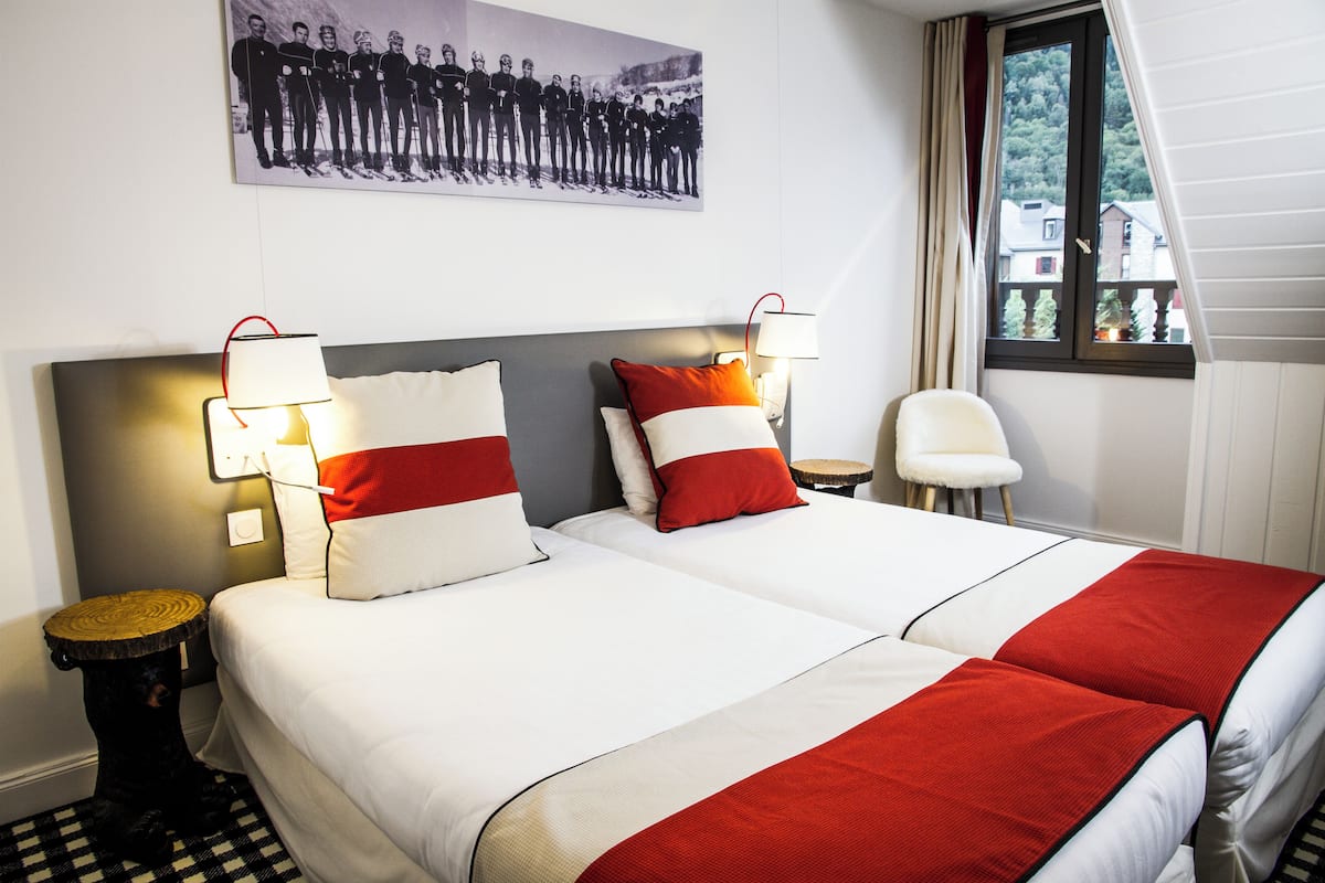 Ein Hotelzimmer mit zwei Betten, einem Kopfteil, Nachttischlampen, einem kleinen runden Tisch und einem Sessel.