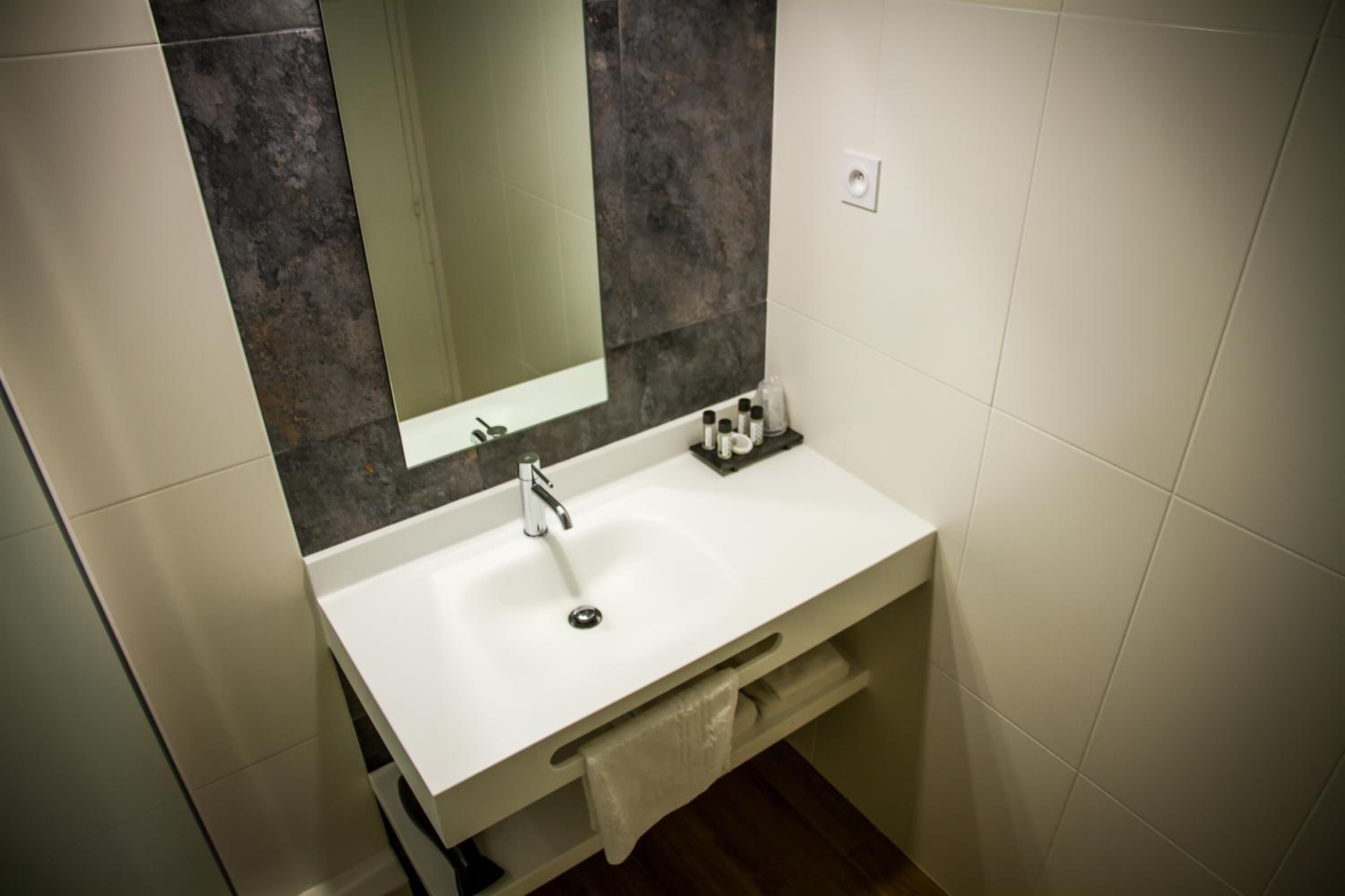 Un baño moderno con un lavabo blanco, un espejo y una pared de azulejos oscuros.