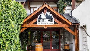 Entrada d'hotel amb façana de fusta, un rètol que diu "HOTEL MIR" i una zona de recepció visible a través de les portes de vidre.