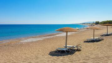 A beach with sun loungers and thatched umbrellas.