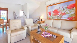 A living room with a sofa, two armchairs, a coffee table, and a painting of flowers. - Holiday home in Kiotari with a terrace (Kiotari)