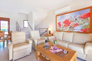 A living room with a sofa, two armchairs, a coffee table, and a painting of flowers.