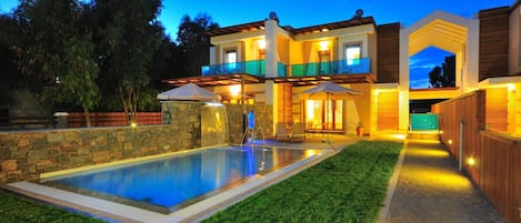 Une maison moderne à deux étages, dotée d’une piscine, d’un espace salon extérieur et d’un patio bien éclairé.