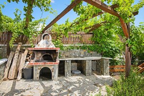 Zona de barbacoa d'exterior amb pedra, un forn de pedra, una pèrgola de fusta i una paret de pedra.