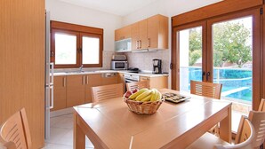 A modern kitchen with wooden cabinets, a dining table with chairs, and a view of a swimming pool. - Holiday home in Kiotari with a terrace (Kiotari)