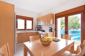 A modern kitchen with wooden cabinets, a dining table with chairs, and a view of a swimming pool.