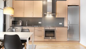 A modern kitchen with wooden cabinets, stainless steel appliances, a dining table with chairs, and a pendant light. - Downtown Apartment by Old Harbor (Reykjavík)