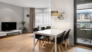 A modern hotel room with a white dining table, black chairs, a flat-screen TV, a potted plant, and a large window with curtains. - Downtown Apartment by Old Harbor (Reykjavík)