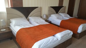 Two single beds with white linens and orange throw blankets, a bedside table with a lamp, and a wooden headboard. - Baku Sea View Hotel (Baku)