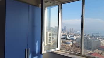 A room with a large window offering a view of a cityscape, including buildings and a body of water.