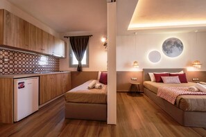 Ein kleines Zimmer mit Küchenzeile, zwei Betten, einem kleinen Tisch und einer runden Wandleuchte.