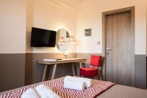 A hotel room with a bed, a desk with a chair, a television, and a door.