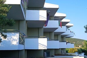 A multi-story building with balconies, a visible air conditioning unit, and a clear sky.