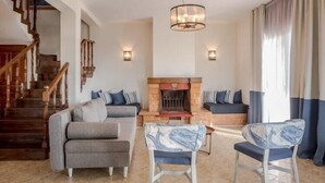 A spacious living room with a fireplace, a staircase, and a chandelier. - Duplex Gerakini Apartment with Pool (Gerakini)
