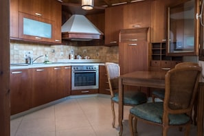 A compact kitchen with wooden cabinets, a built-in oven, and a dining area with a table and chairs.