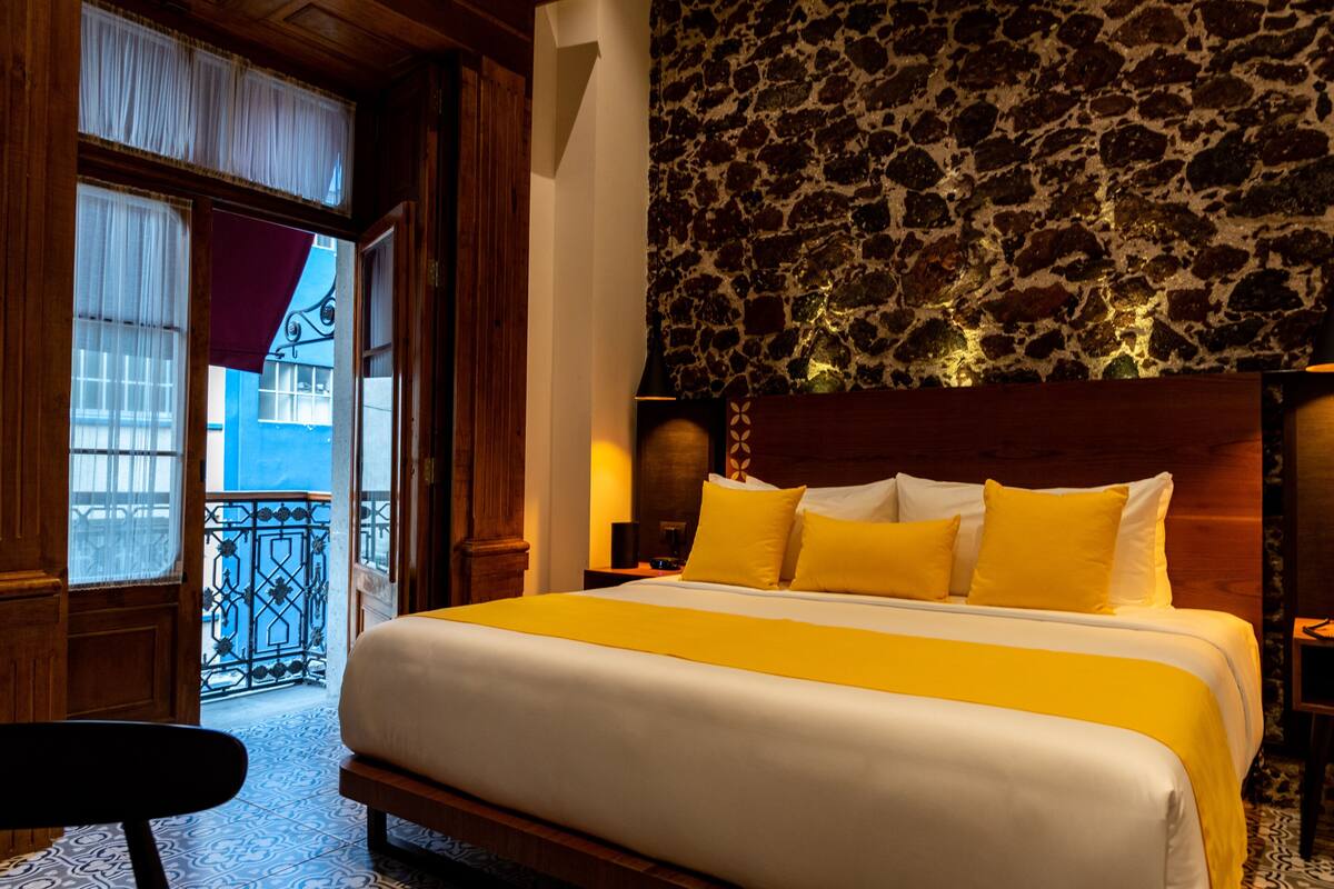 Una habitación de hotel con una cama grande, una pared de piedra y un balcón con barandilla de hierro forjado.