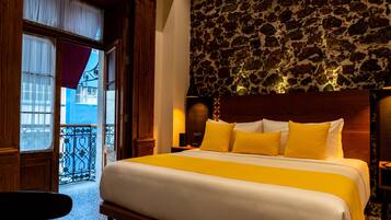 Ein Hotelzimmer mit einem großen Bett, einer Steinwand und einem Balkon mit schmiedeeisernem Geländer.