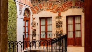 A courtyard with a fountain, a wooden balcony, and a stone wall with a brick pattern.