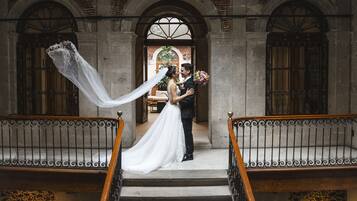 A couple embracing on a staircase with ornate railings and a stone wall in the background.
