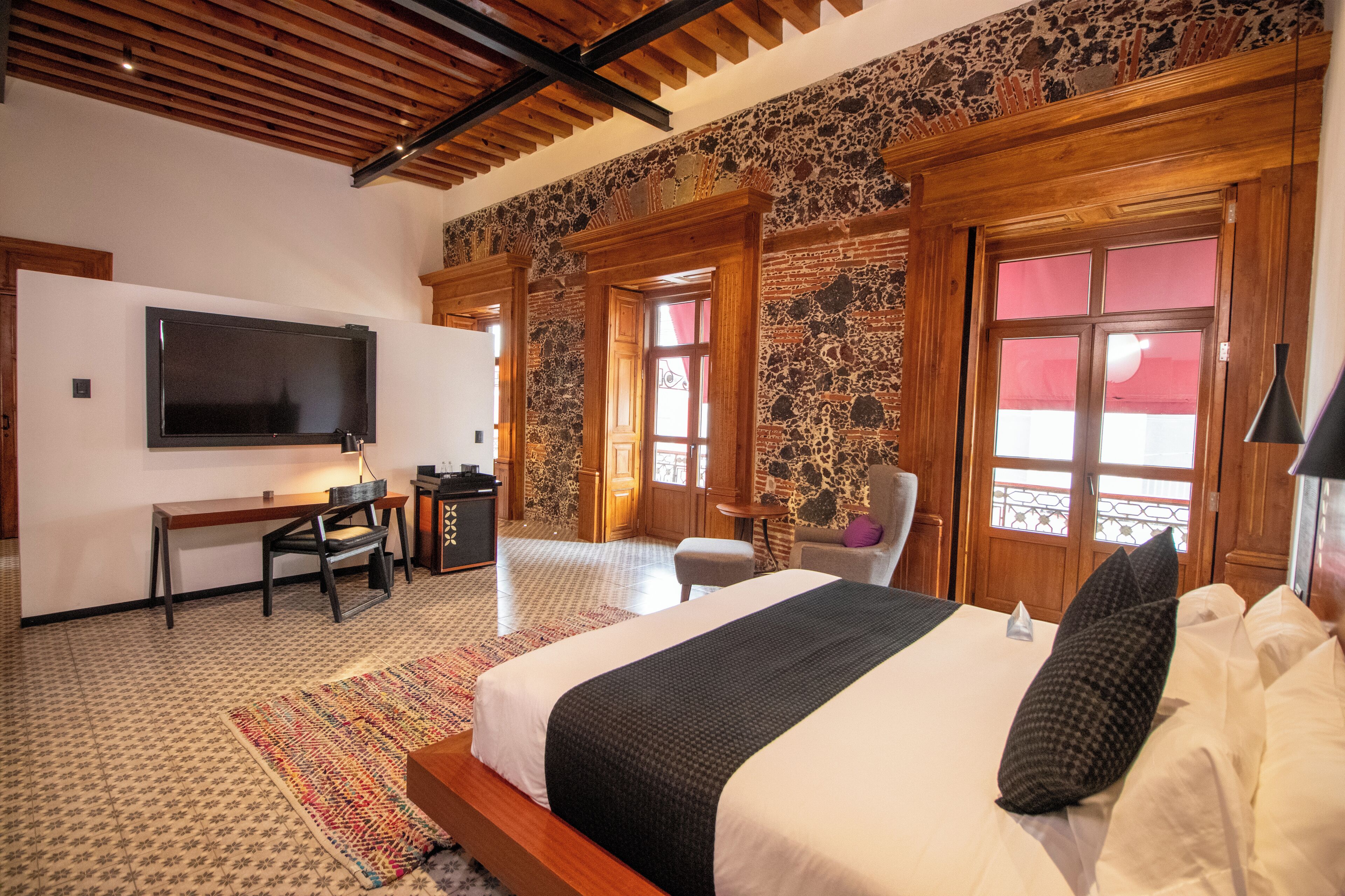 A bedroom with a large bed, a desk with a chair, a TV, and a stone-patterned wall.