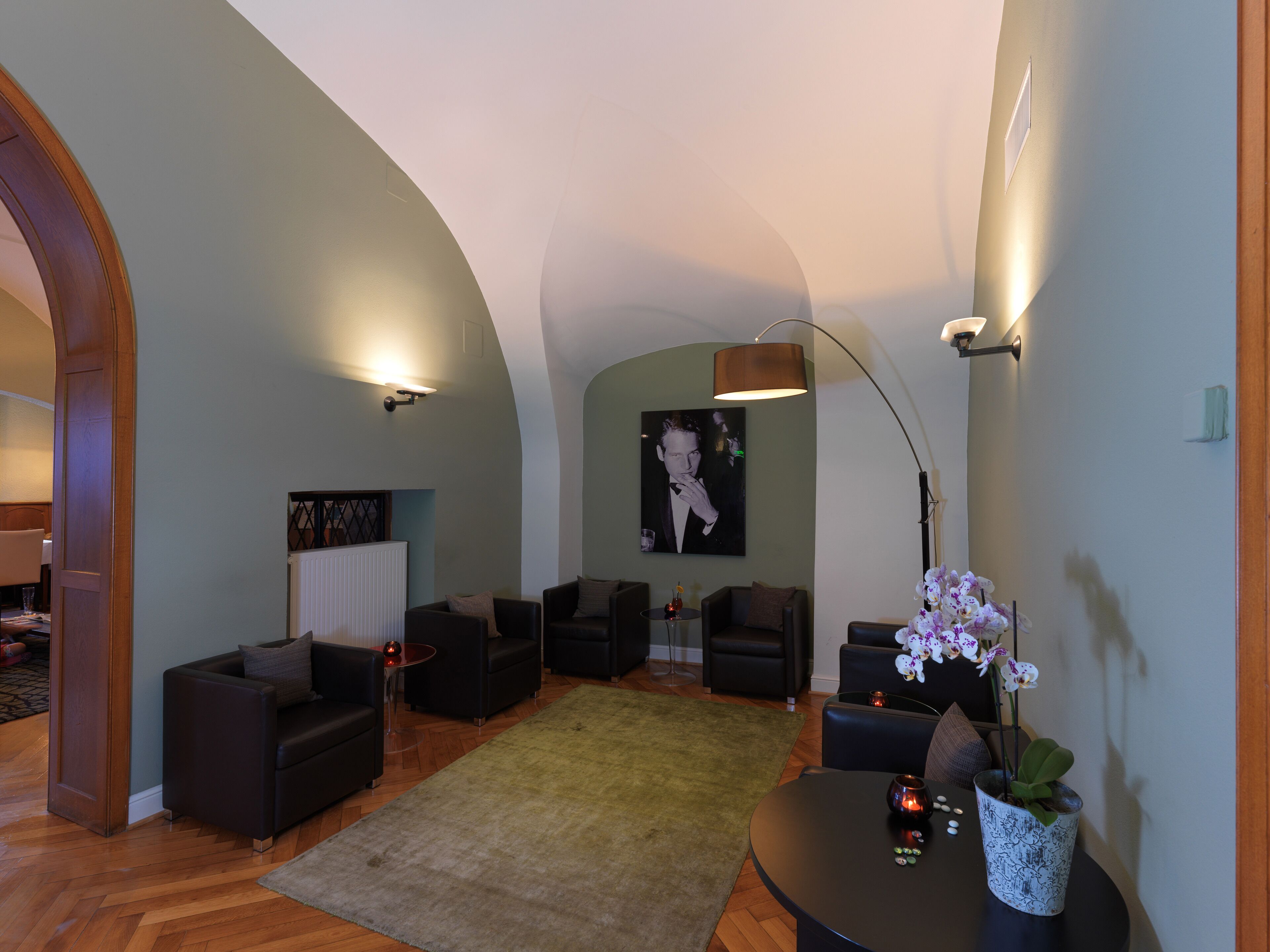 Ein modernes Wohnzimmer mit hohen Decken, dunklen Sofas, einem runden Couchtisch und einem großen Gemälde an der Wand.