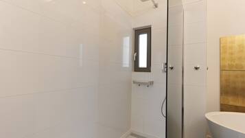 A modern bathroom with a glass shower enclosure, a white sink, and a small window.