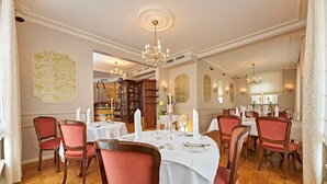 A formal dining room with a round table set for six, surrounded by red upholstered chairs. - Lodner Genießerhotel Drei Mohren (Lauingen)