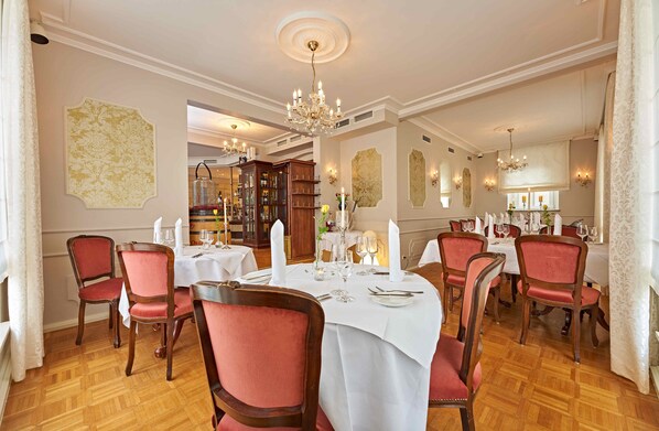 A formal dining room with a round table set for six, surrounded by red upholstered chairs.